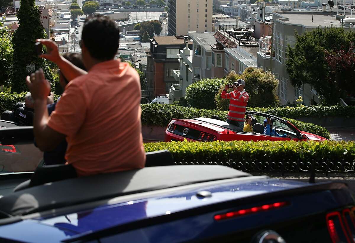 Tourists take pictures while driving down Lombard Street in San Francisco, Calif.