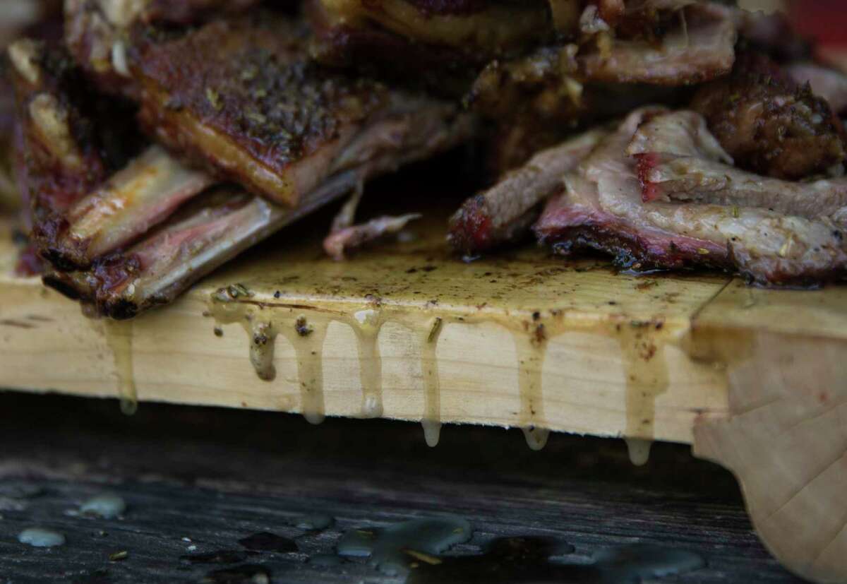 Grease of from the smoked lamb ribs drips off of a cutting board.