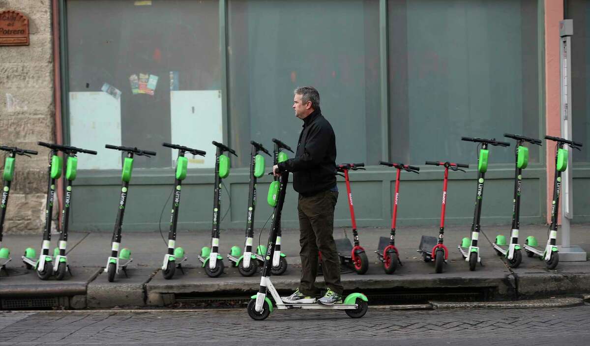 A scooter user rides past a row of scooters on Commerce Street in 2018. Scooters have rapidly made their presence felt in downtown San Antonio. The City Council plans to narrow the firms allowed to operate here to just three. (Kin Man Hui/San Antonio Express-News)