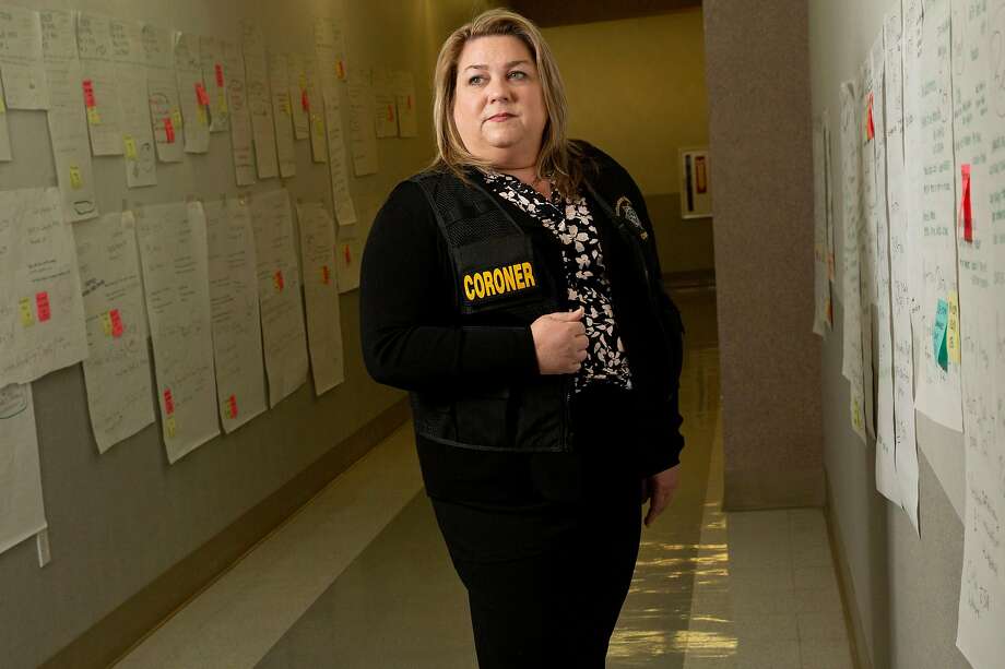 A portrait of Sacramento County Coroner Kimberly Gin on Tuesday, Feb. 19, 2019, in Sacramento. Since the 2018 Camp Fire, Gin and her team use the walls in this Sacramento County Coroner's Office hallway to keep information organized to identify the people killed in the fire. Each poster represents a person. The posters on Gin's left are of those still unidentified. Photo: Santiago Mejia / The Chronicle