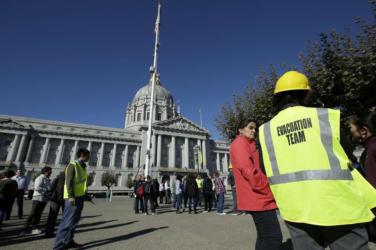 An evacuation team member stands with participants during an earthquake preparedness drill across the street from City Hall in San Francisco, Thursday, Oct. 17, 2019. Earthquake early warning alerts will become publicly available throughout California for the first time this week, potentially giving people time to protect themselves from harm, the Governor's Office of Emergency Services said Wednesday. (AP Photo/Jeff Chiu)