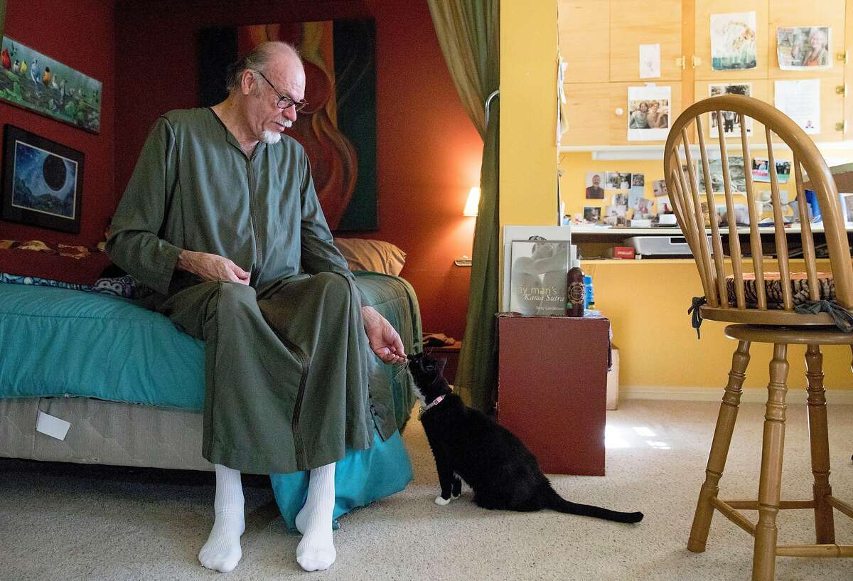 Intersex activist David Cameron Strachan gives his cat Domino a treat while seated on his bed inside his studio in the Mission District of San Francisco, Calif. Friday, Nov. 1, 2019.