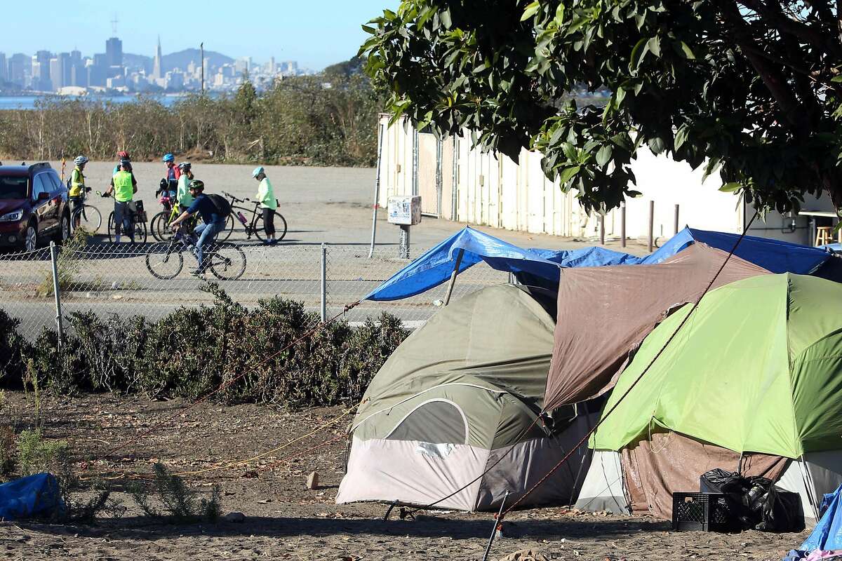 Tents sit on property owned by Caltrans as cyclists and the San Francisco skyline are seen behind them on Tuesday, October 22, 2019 in Berkeley, Calif.