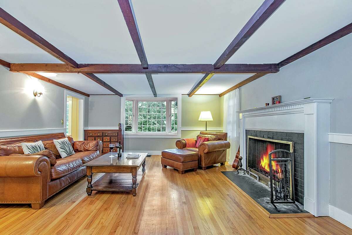 The sizable living room features thick chair railing, a bay window, a ceiling of exposed beams, and a fireplace.
