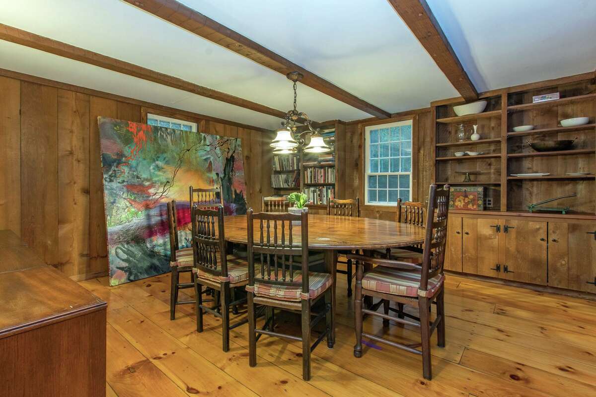 In the formal dining room there are wood-paneled walls, wide-board pine wood flooring, built-in cabinetry and shelving, exposed beams, a window seat, and a dry bar area.