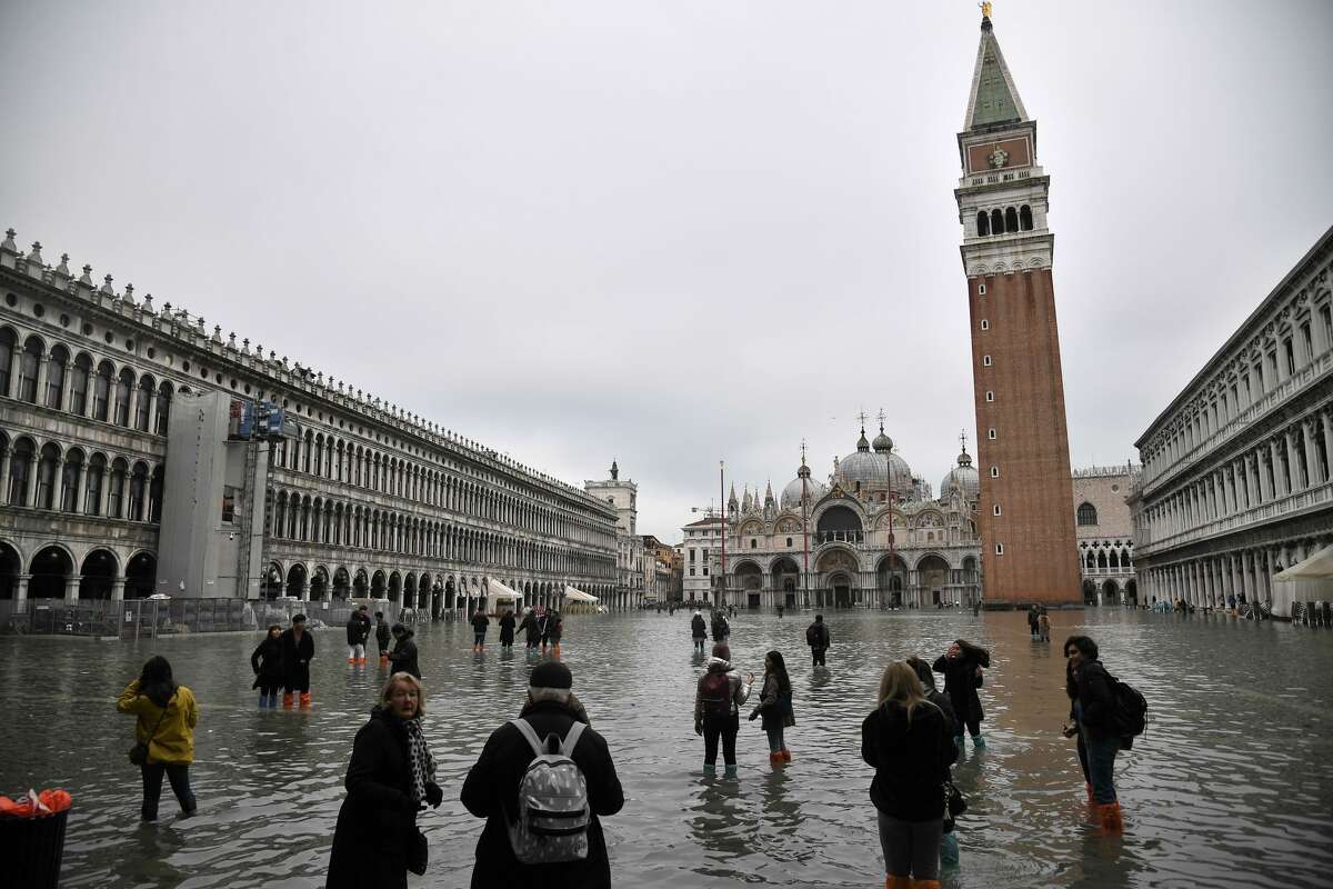 People walk across the flooded St. Mark's square, with St. Mark's basilica and the Bell Tower in background, after an exceptional overnight "Alta Acqua" high tide water level, on November 13, 2019 in Venice. - Venice was hit by the highest tide in more than 50 years late November 12, with tourists wading through flooded streets to seek shelter as a fierce wind whipped up waves in St. Mark's Square.