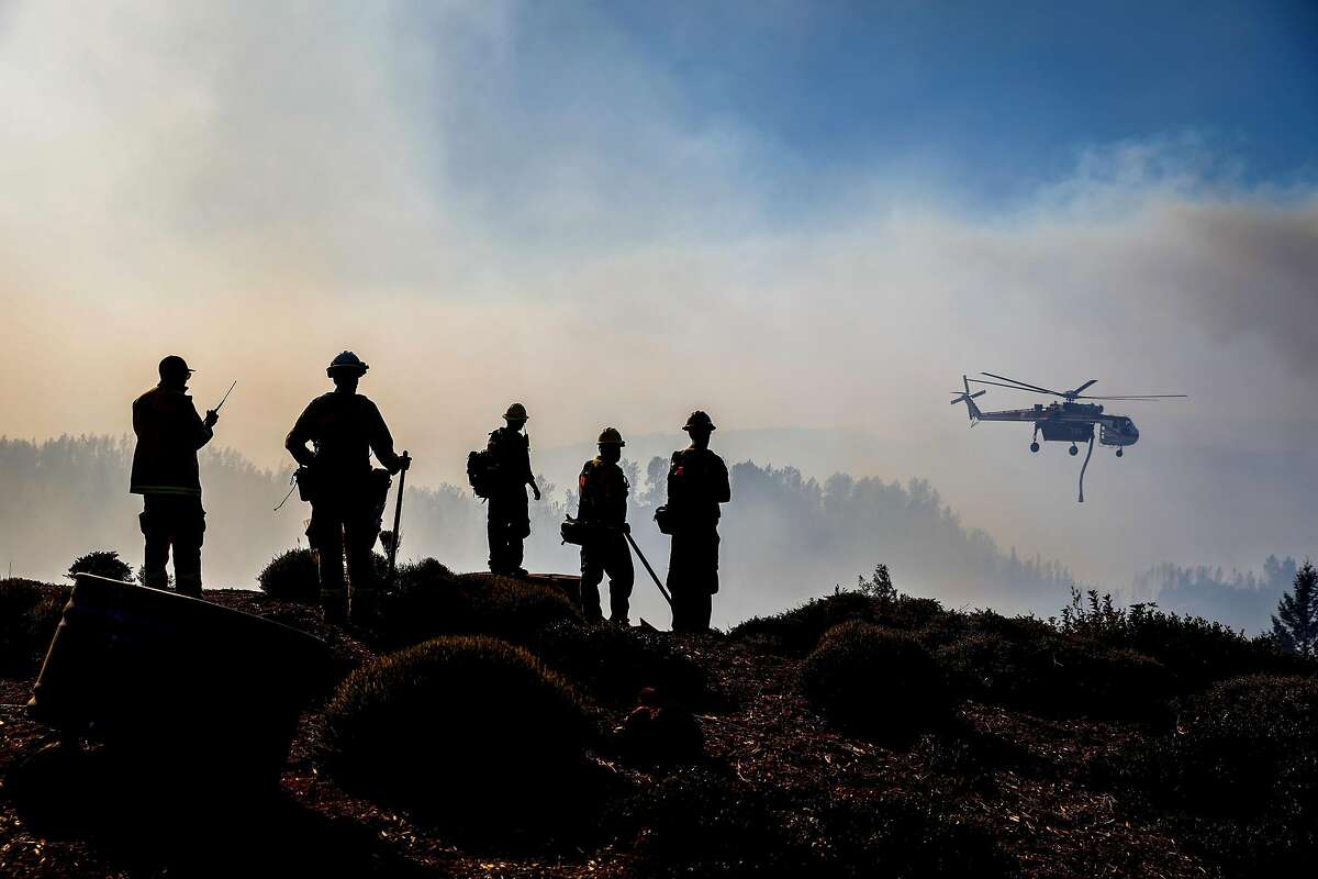 Firefighters watch as a helicopter drops water over the Kincade Fire near Ida Clayton Road in Calistoga, California, on Tuesday, Oct. 29, 2019.
