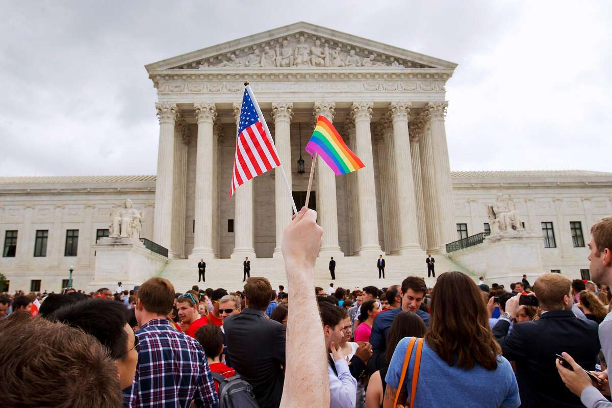 In this Friday June 26, 2015, file photo, a man holds a U.S. and a rainbow flag outside the Supreme Court in Washington after the court legalized gay marriage nationwide. After the decision, religious conservatives are focusing on preserving their right to object. Their concerns are for the thousands of faith-based charities, colleges and hospitals that want to hire, fire, serve and set policy according to their religious beliefs, notably that gay relationships are morally wrong. (AP Photo/Jacquelyn Martin)