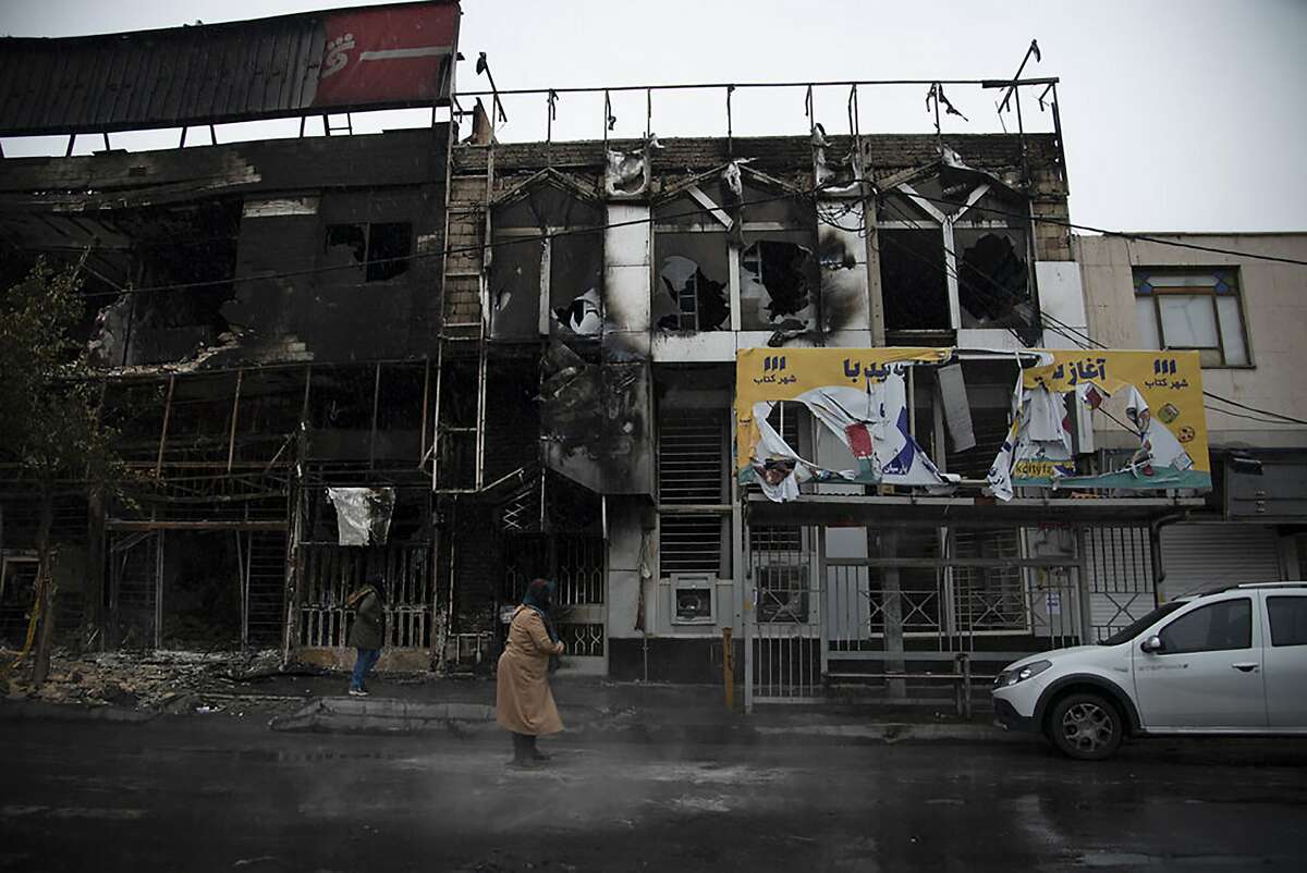 In this photo taken Monday, Nov. 18, 2019, and released by Iranian Students' News Agency, ISNA, people walk past buildings which burned during protests that followed the authorities' decision to raise gasoline prices, in the city of Karaj, west of the capital Tehran, Iran. An article published Tuesday in the Keyhan hard-line newspaper in Iran is suggesting that those who led violent protests will be executed by hanging as the unrest continues. (Masoume Aliakbar/ISNA via AP)