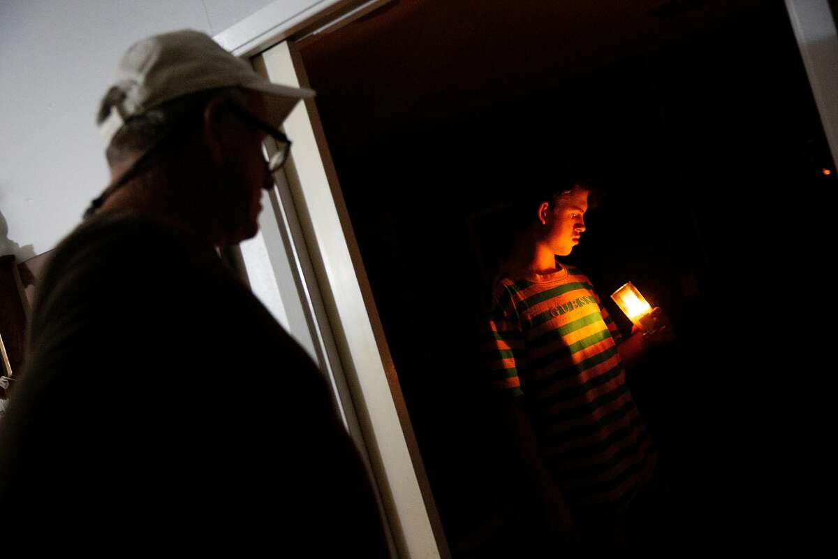 From left: William Douglas Hitt watches as his son Connor Hitt, 17, lights a candle at his home as light from a flashlight illuminates the kitchen area on Wednesday, Nov. 20, 2019, in St. Helena, Calif. The power is out at his neighborhood off of Spring Street. PG&E has shut off the power to more than 40,000 homes in an effort to prevent wildland fires.