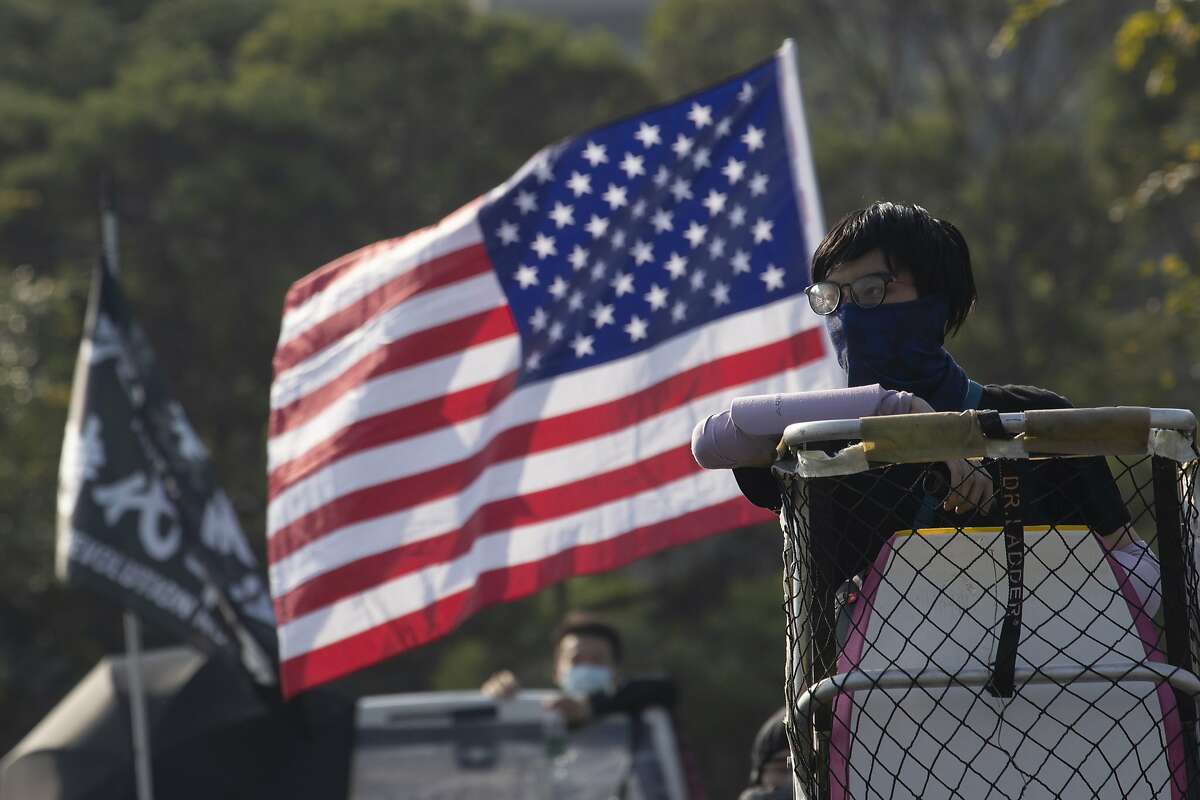 A protester watch from a lookout position near a U.S. flag on the barricaded bridge into the Chinese University of Hong Kong, in Hong Kong, Wednesday, Nov. 13, 2019. Protesters in Hong Kong battled police on multiple fronts on Tuesday, from major disruptions during the morning rush hour to a late-night standoff at a prominent university, as the 5-month-old anti-government movement takes an increasingly violent turn. (AP Photo/Ng Han Guan)