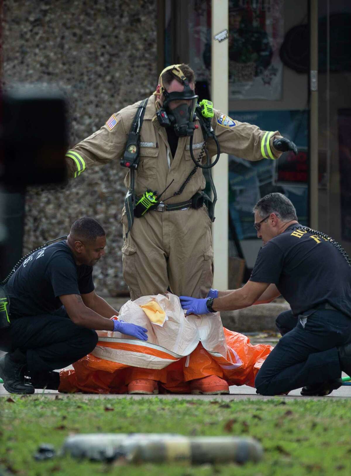 Houston Firefighters help investigators remove the hazmat suit after walked out of the building at 6100 block of West 34th Street on Thursday, Nov. 21, 2019, in Houston. Multiple agencies, including FBI, Houston Police Department, Houston Fire Department and Drug Enforcement Administration officials were working together at the scene.