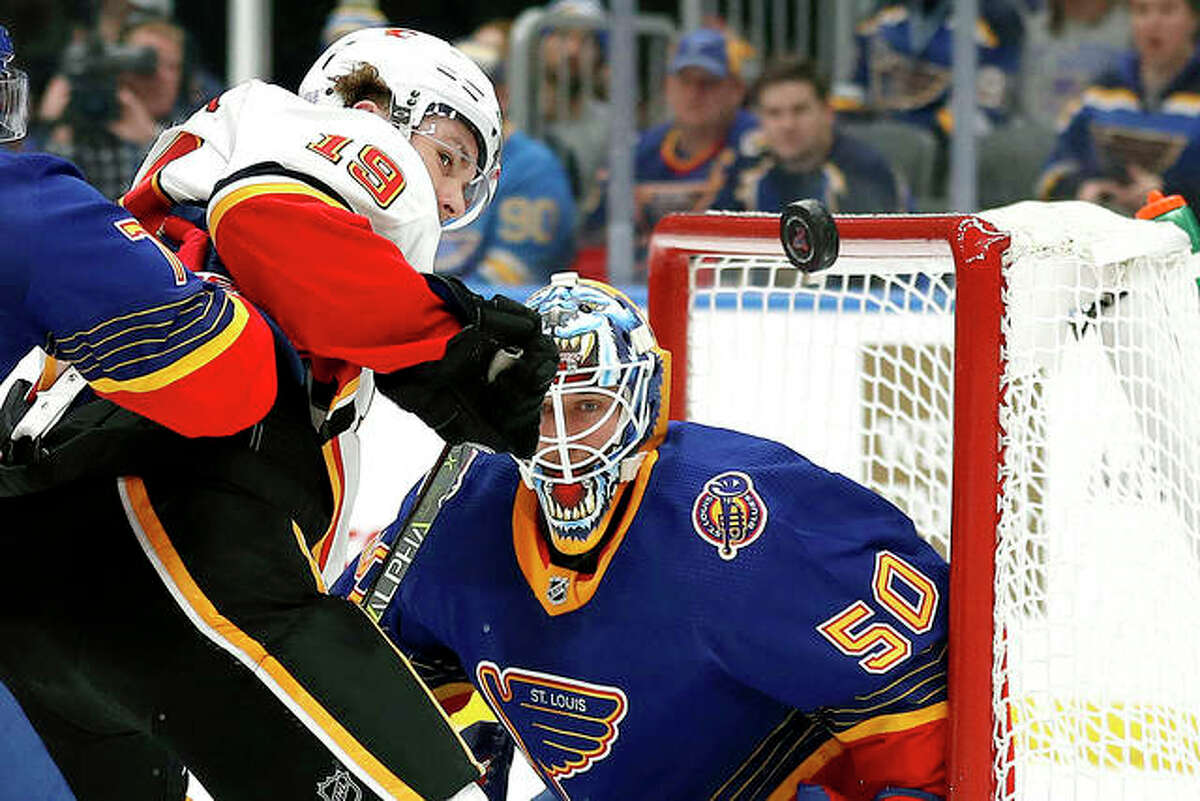 The Flames’ Matthew Tkachuk (19) and Blues goaltender Jordan Binnington watch the puck in the air in the third period of Thursday night’s game in St. Louis. The Blues won 5-0.