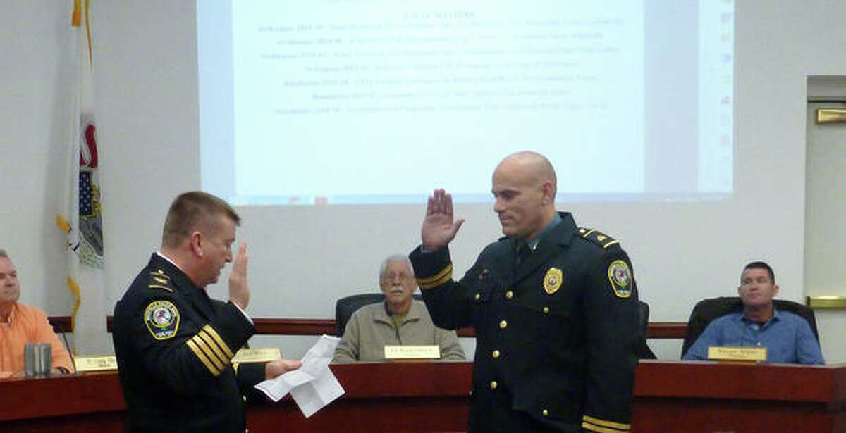 Maryville Chief of Police Rob Carpenter, left, swears in his new deputy chief, Tony Manley, during Wednesday’s village trustee board meeting. In the background are the mayor and various trustees.