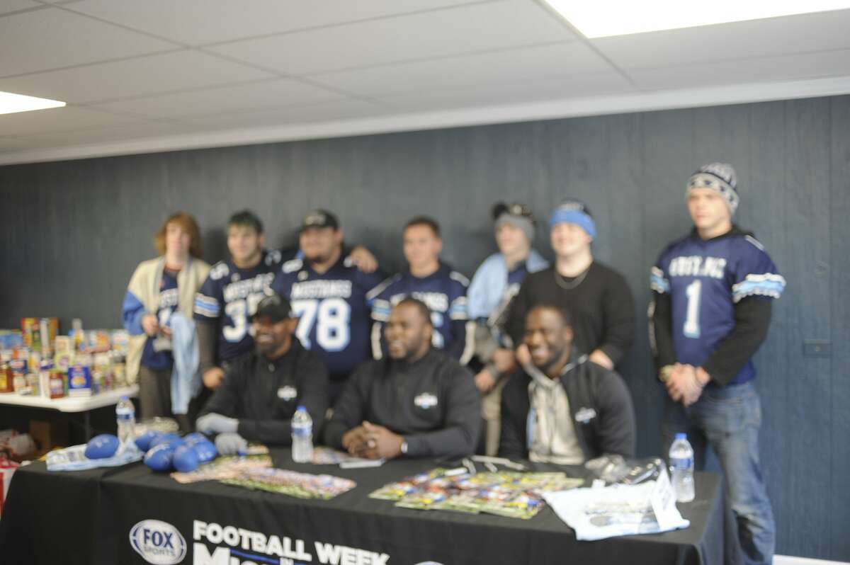 A group of students poses for a photo with former Detroit Lions receiver Herman Moore (seated, left), former Lions running back Joique Bell (center) and former Michigan quarterback Devin Gardner (right). The three athletes were at the Midland County Emergency Food Pantry on Friday afternoon to meet the public and to promote food drives both at the food pantry and at Kroger later that day.