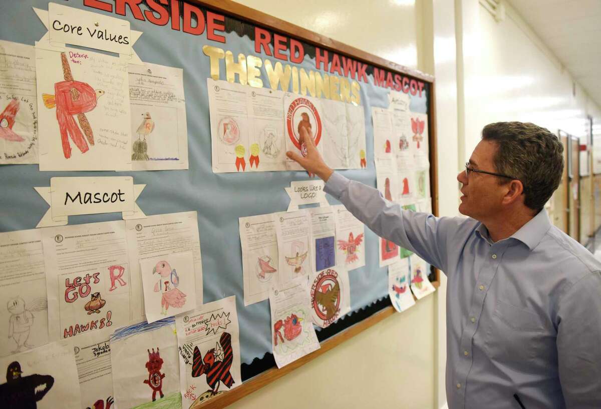 School Principal Chris Weiss shows student logo designs from the Riverside Red Hawk mascot contest on display at Riverside School in the Riverside section of Greenwich, Conn. Tuesday, Nov. 19, 2019. The school, which used a raccoon as its mascot a long time ago, is rebranding with a red hawk as its new mascot and held a contest for students to have a say in the design of the new logo.