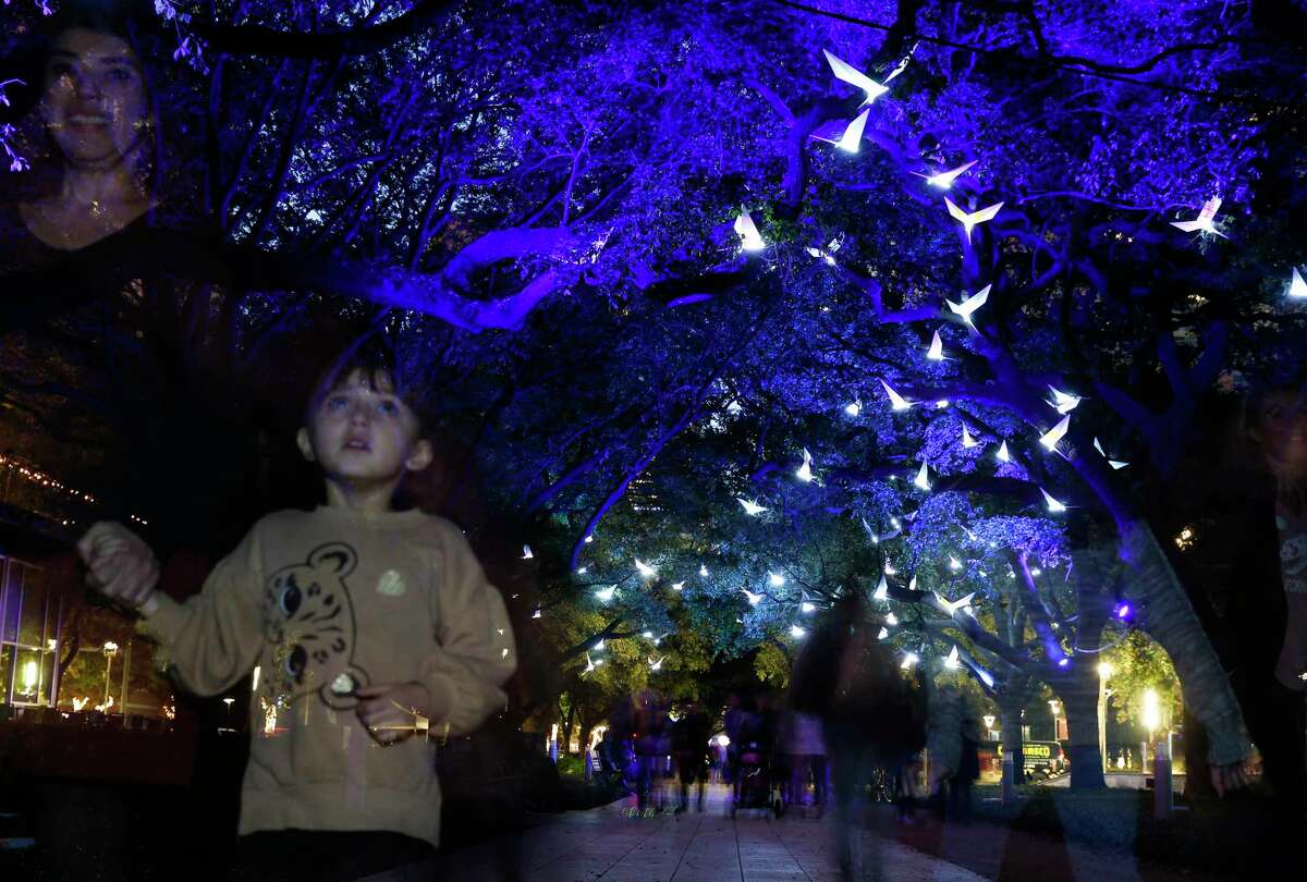 People walk under Discovery Green's holiday exhibit "Paloma" a sound and light exhibit along the Oak Allee on Sunday, Nov. 24, 2019 in Houston. This year's holiday installation combines a soundtrack by Houston artist Lina Dibb that incorporates the calls of migratory birds with the French collective Pitaya's 200 lighted, origami-like, white steel bird forms that appear to be flying through the tree canopy.