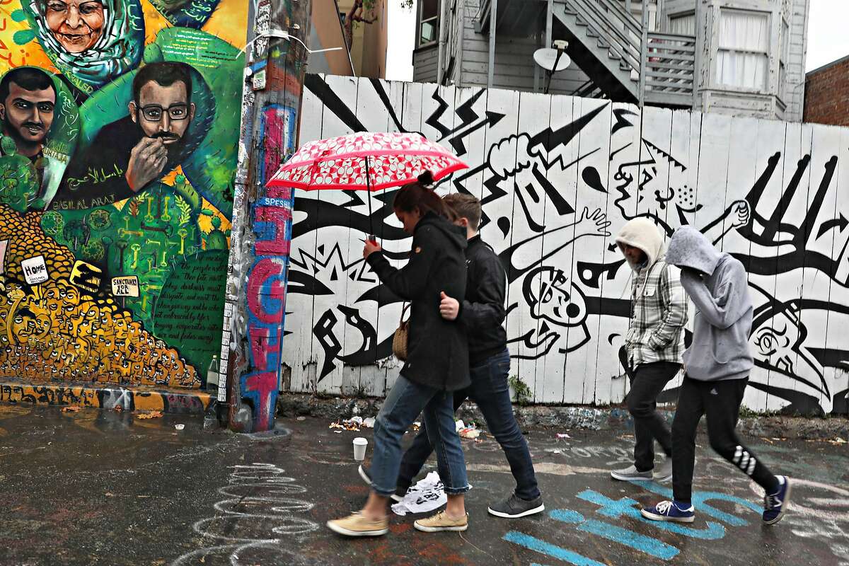 Rain starts as Zack Rosenfeld and his girlfriend M\adi Mamoone (left) from Rochester, NY, and family (behind) from different areas get together for Thanksgiving week as they take a walk on Clarion Alley viewing murals seen on Tuesday, Nov. 26, 2019, in San Francisco, Calif.