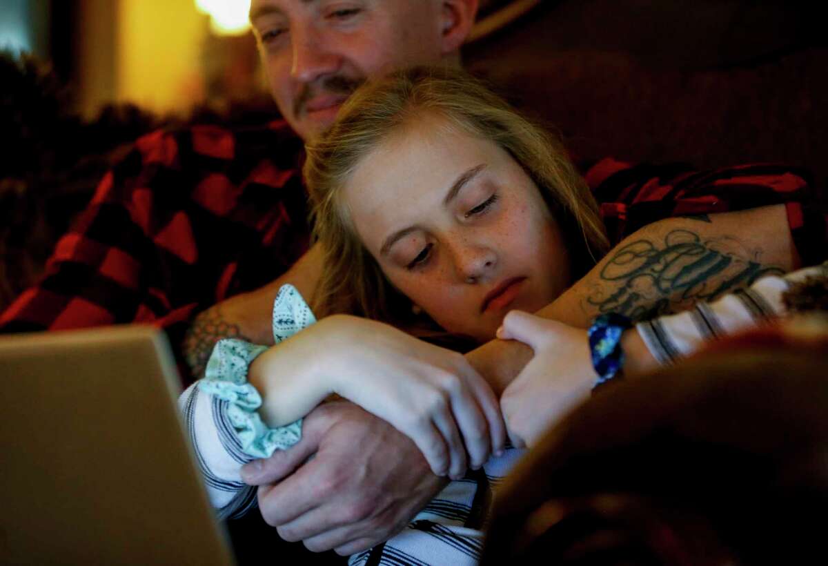 Peyton, 10, examines her father's, Kenyon Saylor White, arm while watching a YouTube show on Sunday, Nov. 24, 2019, in Katy, Texas.