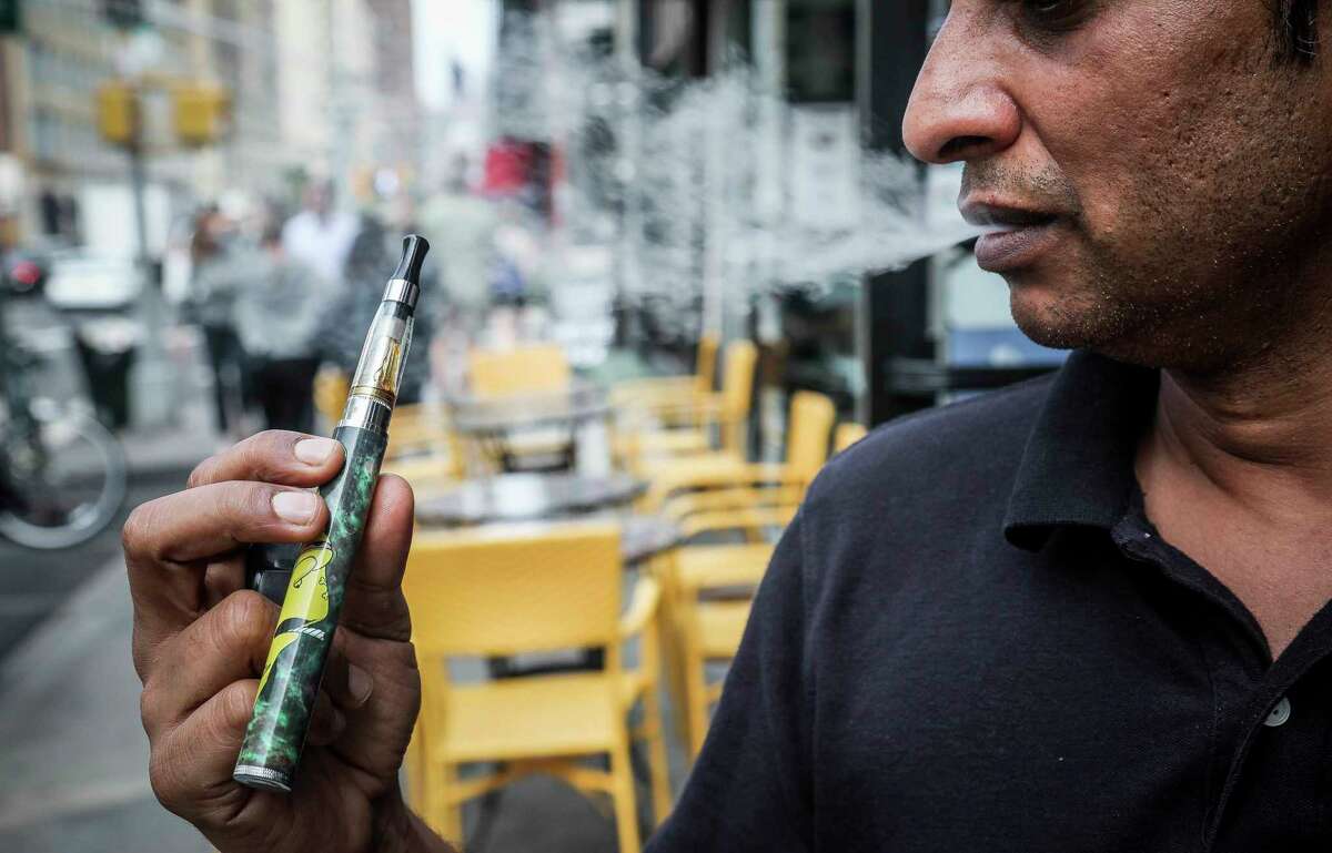 FILE - In this Sept. 16, 2019 file photo, Inam Rehman, manager of Jubilee Vape & Smoke Inc., vapes in New York. City lawmakers are poised to enact a ban on flavored e-cigarettes Tuesday, Nov. 26, 2019. (AP Photo/Bebeto Matthews, File)