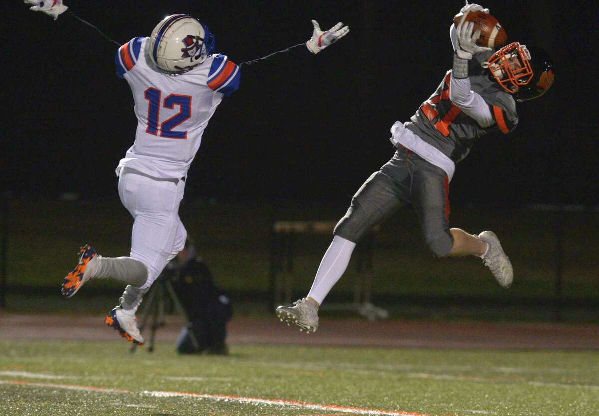 Ridgefield's Owen Gaydos (21) pulls in a pass while being defended by Danbury's Deaven Smith (12) in the football game between Danbury and Ridgefield high schools. Wednesday night, November 27, 2019, at Ridgefield High School, Ridgefield, Conn. Gaydos turned and ran it in for a touchdown.
