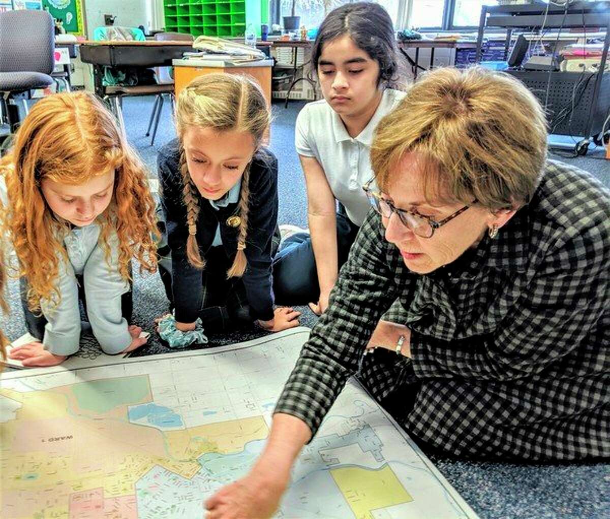 From left, Blessed Sacrament School fifth-graders Lindsay Hofmeister, Payton Mathe and Marina Cruz-Wild look on as Mayor Maureen Donker highlights various areas on a map of Midland. (Photo provided)