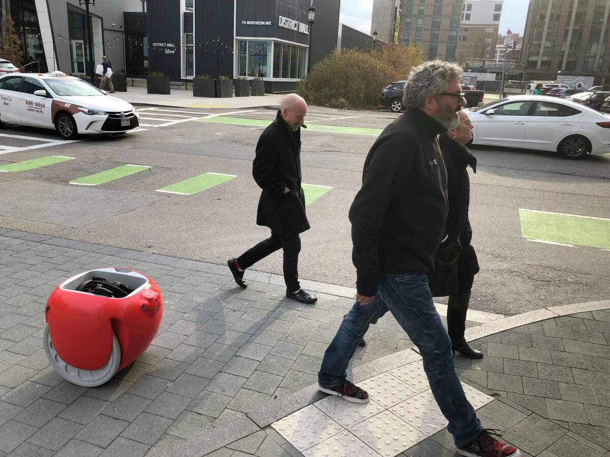 Piaggio Fast Forward CEO Greg Lynn, center, is followed by his company's Gita carrier robot as he crosses a street on Monday, Nov. 11, in Boston. The two-wheeled machine is carrying a backpack and uses cameras and sensors to track its owner. (AP Photo / Matt O'Brien)