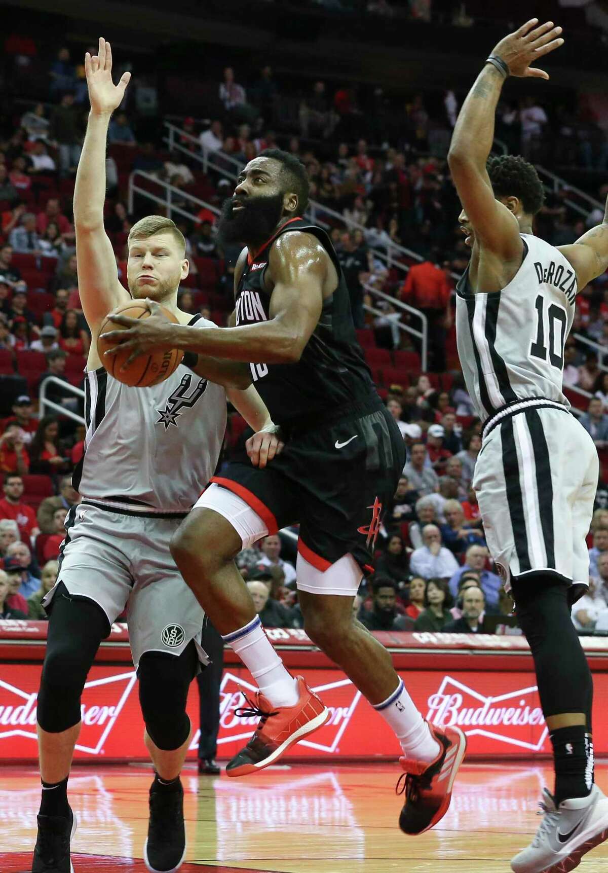 Houston Rockets guard James Harden (13) goes toward the basket while San Antonio Spurs players Davis Bertans (42) and DeMar DeRozan (10) are defensing during the first quarter of the NBA game at Toyota Center on Friday, March 22, 2019, in Houston.