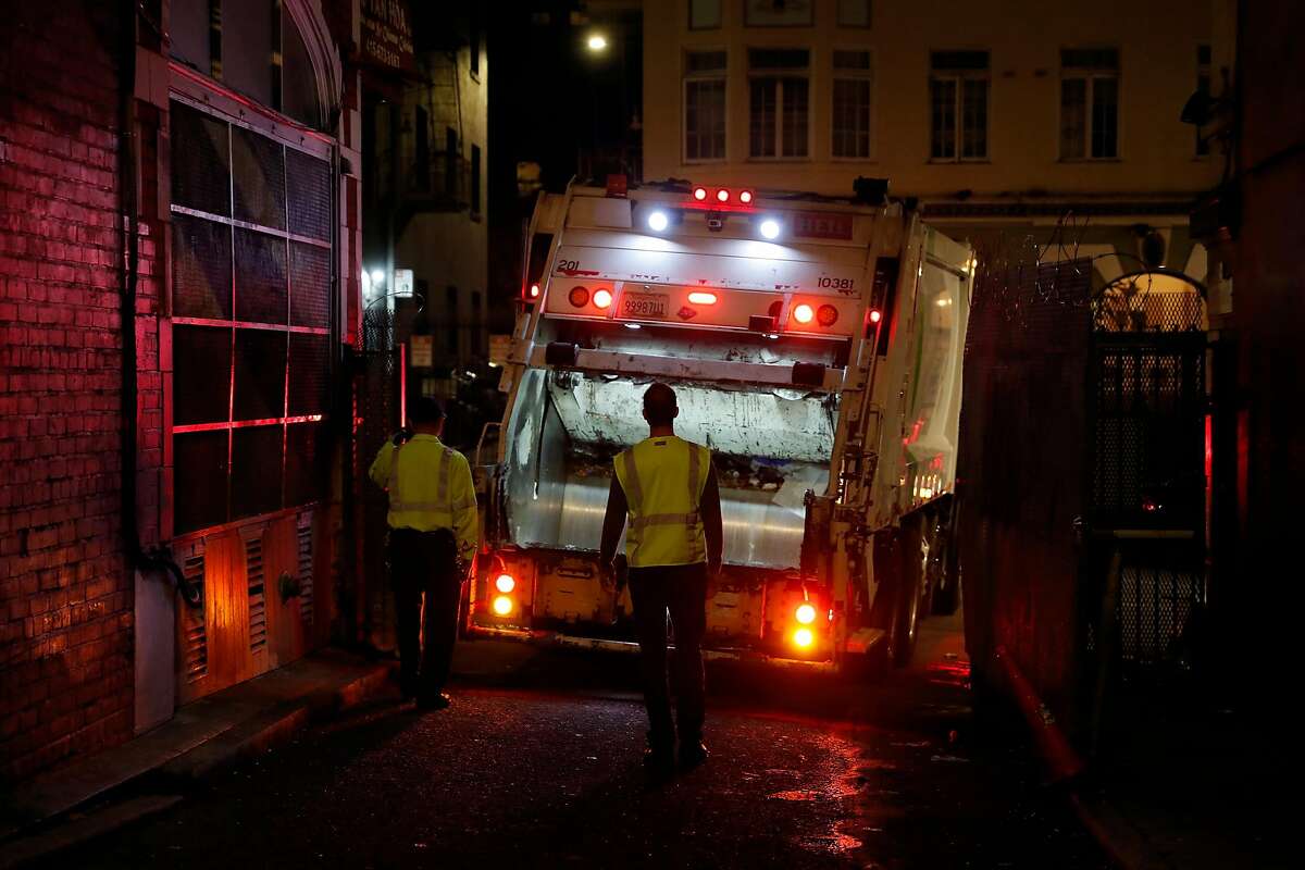 Recology Operations Supervisor Kareem Saber and Ron Reali (left) guide a truck as it backs into Antonio Alley in the Tenderloin District in San Francisco, Calif., on Tuesday, December 3, 2019.