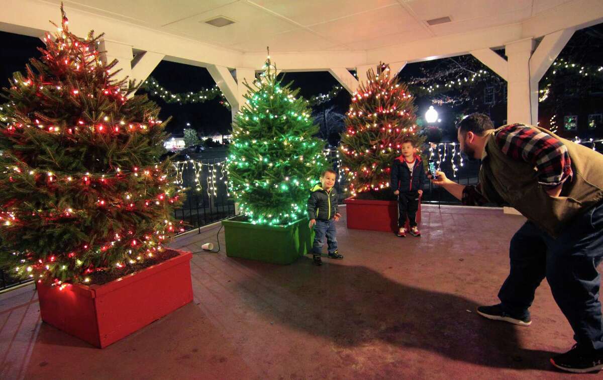 With the lit up Christmas trees as a backdrop, Andrew Picart, of Trumbull, snaps photos of his sons Ethan, 2, and Tyler, 6, during the annual holiday tree lighting event at Town Hall Green in Trumbull, Conn., on Friday Dec. 6, 2019.