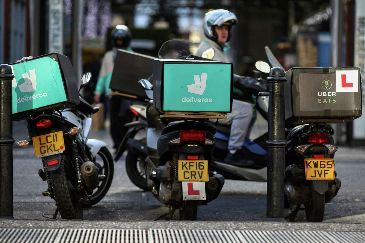 Motor scooters with boxes for Deliveroo stands next to a motor scooter with a box for UberEats in London on Dec. 22, 2016.