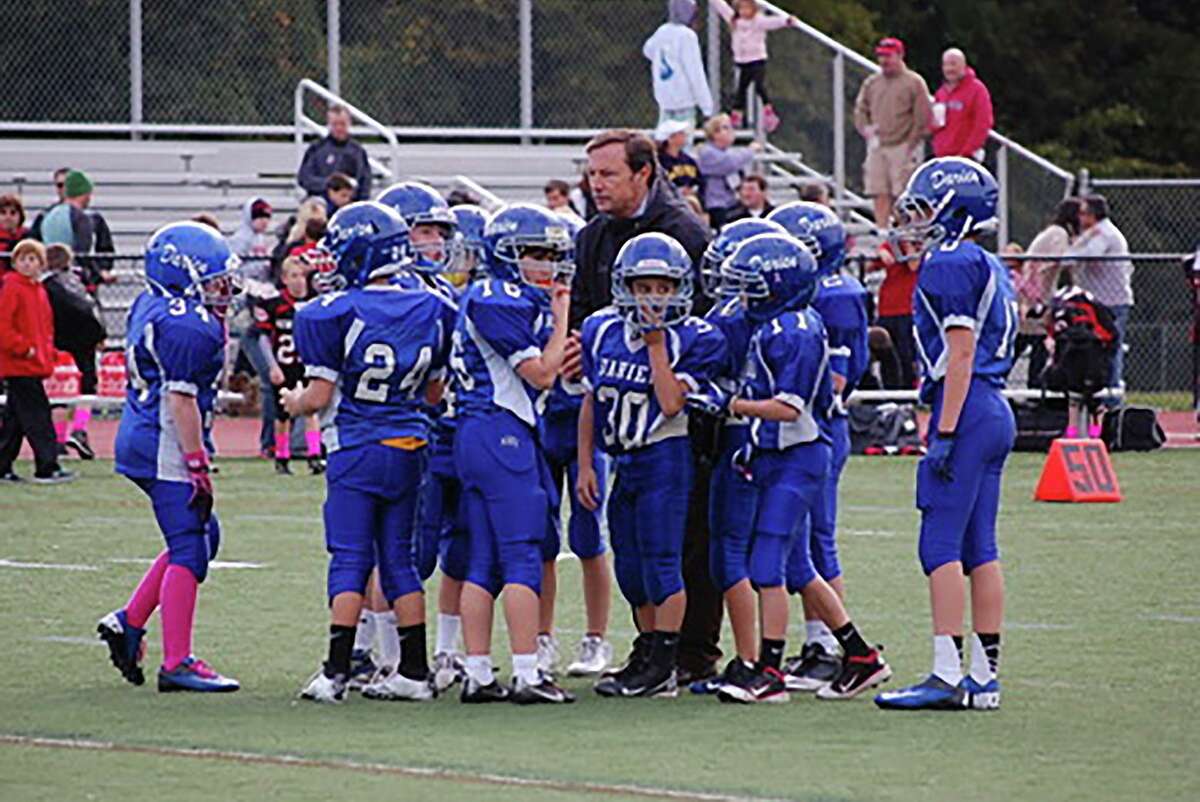 Darien High School football coach Rob Trifone in the huddle with the Darien Junior Football League's third grade team during the 2010 season. Trifone has coached that group of players for the past 10 seasons, and many are seniors on his 2019 Blue Wave varsity team.