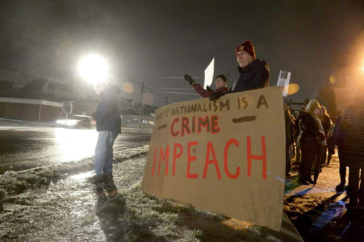 Ed Edelson, right, former First Selectman of Southbury, stands behind a sign as community members rally for the impeachment of President Trump at the corner of Greenwood Ave and Route 53 on Tuesday evening. December 17, 2019, in Bethel, Conn.