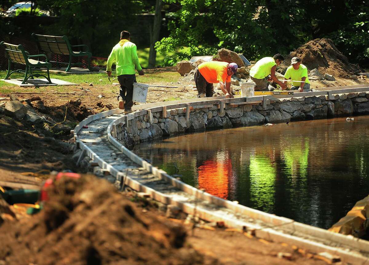 Workers rebuild the stone wall surrounding the duck pond behind City Hall in Milford, Conn. on Thursday, July 5, 2018. The wall reconstruction is part of a larger project that includes the dredging of both the lower and upper duck ponds earlier this year.