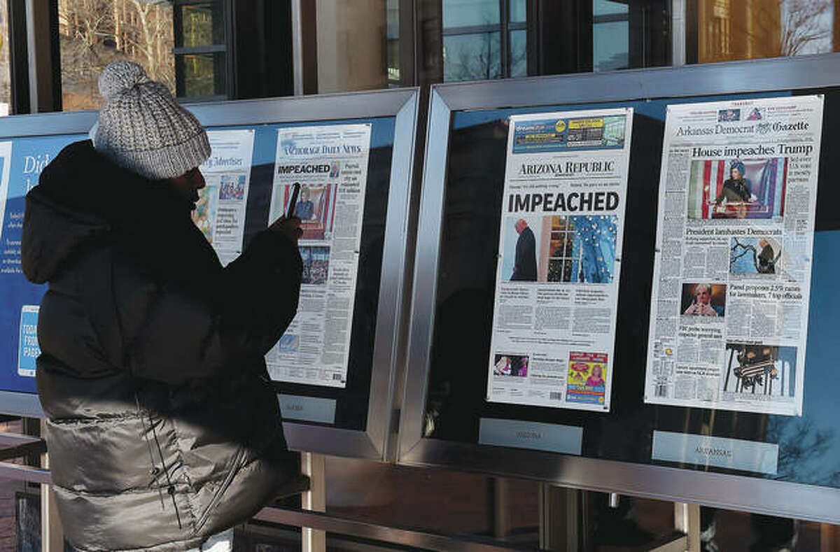 A person takes a picture of newspaper front pages on display at the Newseum in Washington, D.C., on Thursday after President Donald Trump’s historic impeachment by the House of Representatives.