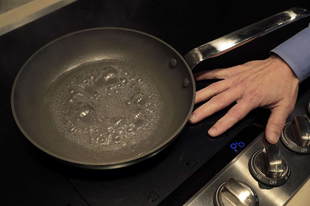 Wei-Tai Kwok places his hand on an induction cooktop in his kitchen, where he replaced natural gas appliances with electric ones.