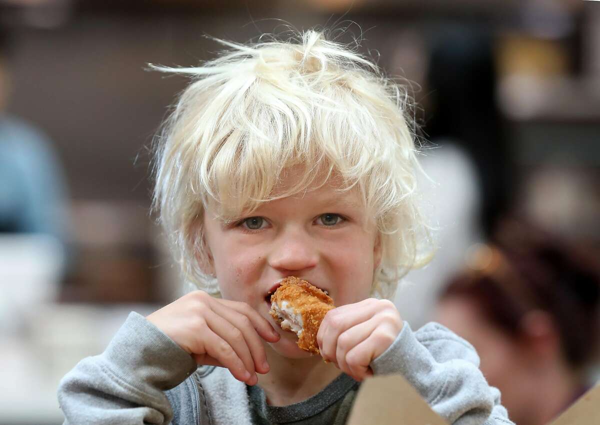 Wilds Moffett, 5 years old, visiting from Oceanside eats chicken from Minnie Bell's Soul Movement at the Public Market on Monday, Dec. 23, 2019, in Emeryville, Calif.
