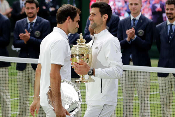 FILE - In this July 14, 2019, file photo, second placed Switzerland's Roger Federer, left, walks past winner Novak Djokovic, of Serbia, during trophy ceremonies after the men's singles final match at the Wimbledon Tennis Championships in London. (AP Photo/Ben Curtis, File)
