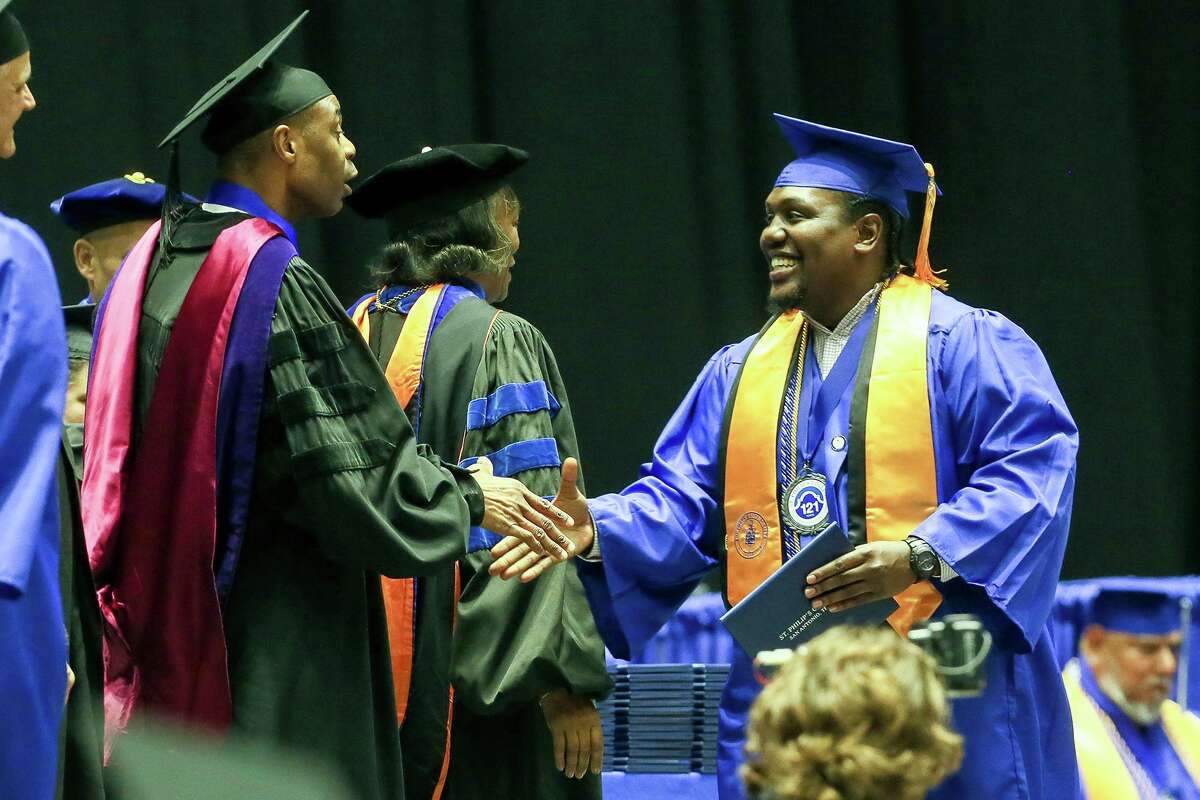 Terrance Johnson, right, shakes the hand of U.S. District Judge Jason Pulliam as he crosses the stage with his diploma at graduation ceremonies for St. Philip's College at Freeman Coliseum on Dec 13. Johnson, who is homeless, was the student graduation speaker and received an associate's degree in teaching.
