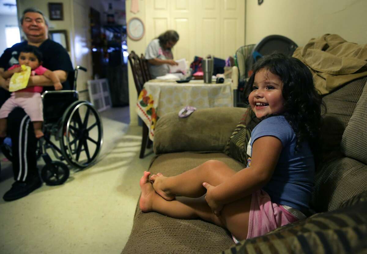 Joe Garcia, left, holds his granddaughter Ashley as his other granddaughter Izabella, 3, sits on the sofa. Joe and his wife Teresa Garcia are raising their grandchildren in their apartment, but they were almost evicted this summer.