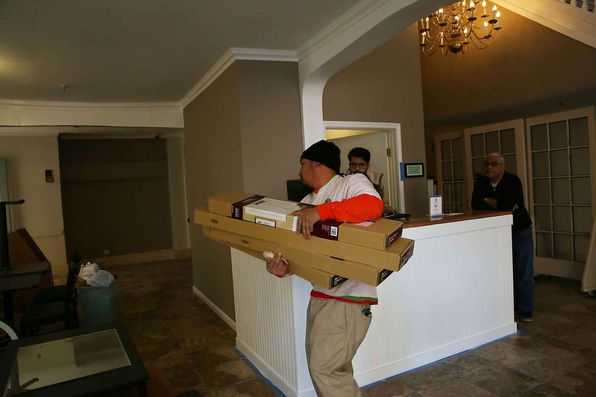 Artemio Diaz (l to r), laborer 3 Mac, carries supplies through the lobby while Alpesh Parek, front desk, and Dave Patel, manager, work together at the front desk at the Abigail Hotel on Monday, January 6, 2020 in San Francisco, Calif.