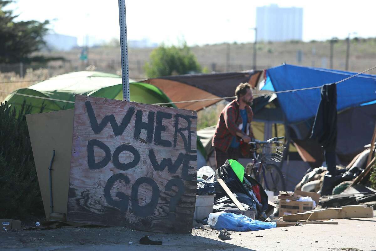 A sign reading “Where do we go?” sits on University Avenue next to a homeless encampment on CalTrans property as one of the residents of the encampment prepares to ride a bike on Tuesday, October 22, 2019 in Berkeley, Calif.
