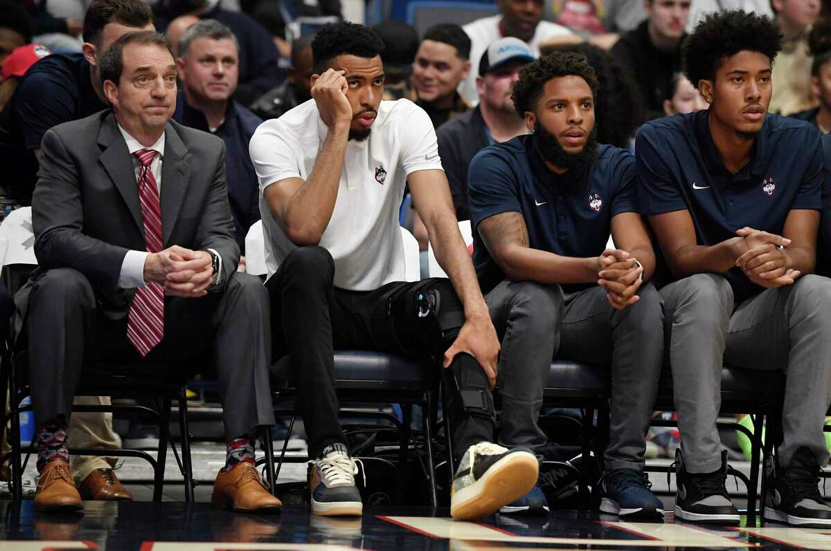 Connecticut’s Tyler Polley, second from left, watches play from the bench in the first half of an NCAA basketball game, Sunday, Jan. 12, 2020, in Hartford, Conn. Polley is out for the season after he tore his left ACL at practice on Friday.