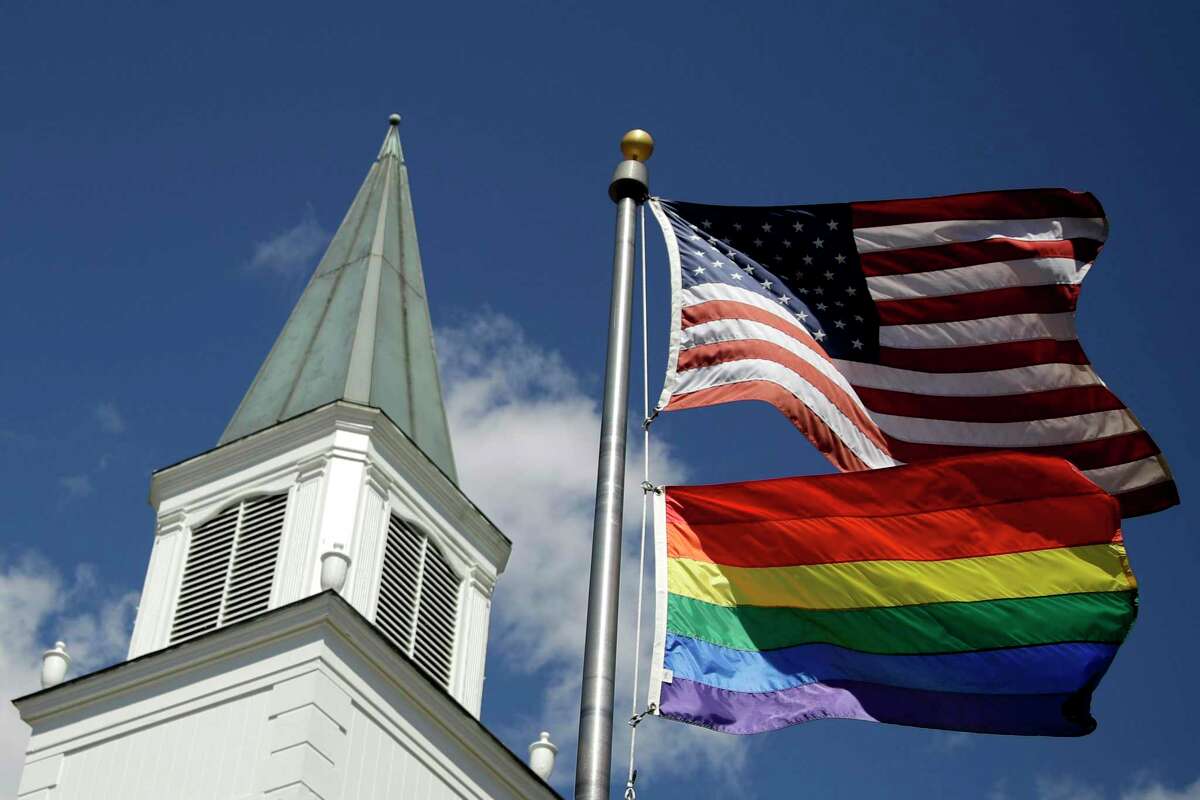 FILE - In this April 19, 2019 file photo, a gay pride rainbow flag flies along with the U.S. flag in front of the Asbury United Methodist Church in Prairie Village, Kan. A new Associated Press-NORC Center for Public Affairs Research poll shows age, education level and religious affiliation matter greatly when it comes to Americans’ opinions on a prospective clergy member’s sexual orientation, gender, marital status or views on issues such as same-sex marriage or abortion (AP Photo/Charlie Riedel)