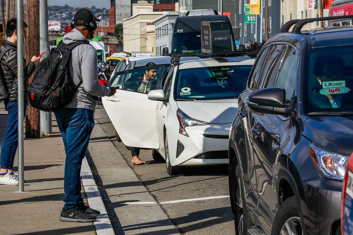 A woman (center) gets into a Lyft car outside the Cal Train station on Townsend Street in San Francisco, California, on Monday, May 20, 2019. Both Uber and Lyft have agreed to a 3.25%-per ride tax in an effort to avoid a tax on their gross receipts. The taxes will generate an estimated $30 million to $35 million for transportation improvements and street-safety upgrades.