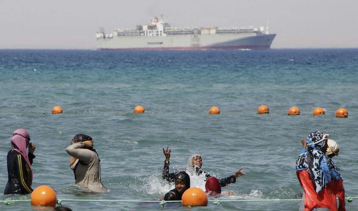 FILE - In this Sunday, Aug. 9, 2015 file photo, a ship crosses the Gulf of Suez towards the Red Sea as holiday-makers swim in Suez, 127 kilometers (79 miles) east of Cairo, Egypt. The Suez Canal, which connects the Red Sea to the Mediterranean Sea, revolutionized maritime travel by creating a direct shipping route between the East and the West. But as Egypt marks the 150th anniversary of its opening, marine biologists are bemoaning one of the famed waterway's lesser known legacies, the invasion of hundreds of non-native species that have driven the native marine life toward extinction and altered the delicate Mediterranean ecosystem with potentially devastating consequences. (AP Photo/Amr Nabil, File)