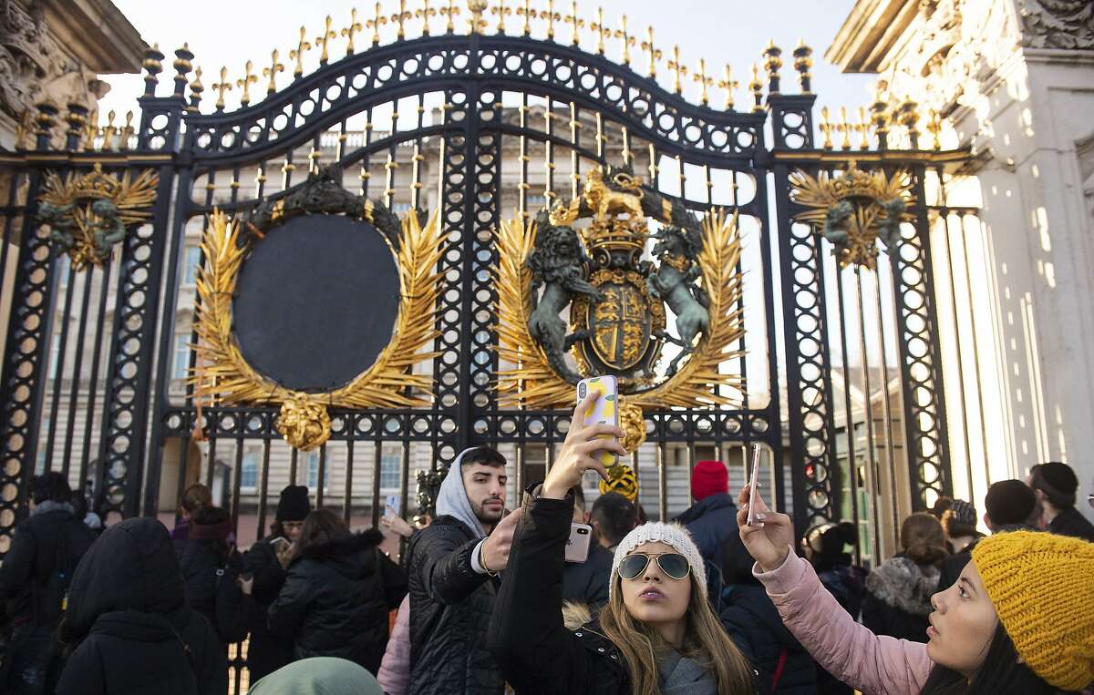 Tourists take photos outside the gates of Buckingham Palace, following a statement by Britain's Queen Elizabeth II and Buckingham Palace, in London, Sunday January 19, 2020. Buckingham Palace says Prince Harry and his wife, Meghan, will no longer use the titles "royal highness" or receive public funds for their work under a deal that allows them to step aside as senior royals. (Dominic Lipinski/PA via AP)