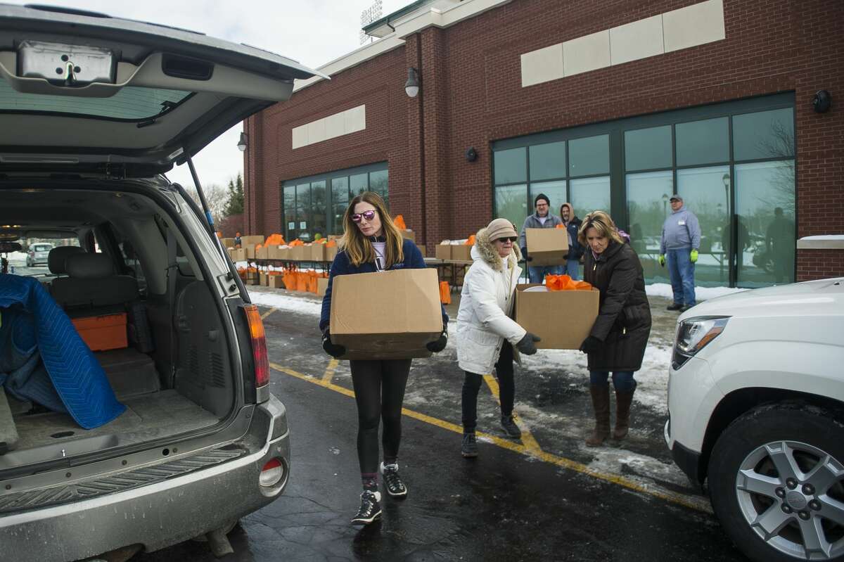 Volunteer Kaly LeBourdais of Saginaw, center, carries a box of food items to a patron's vehicle during a food distribution event hosted by The Arc of Midland, Hidden Harvest and Food Bank of Eastern Michigan in celebration of Martin Luther King Jr. Day Monday, Jan. 20, 2020 at Dow Diamond. (Katy Kildee/kkildee@mdn.net)