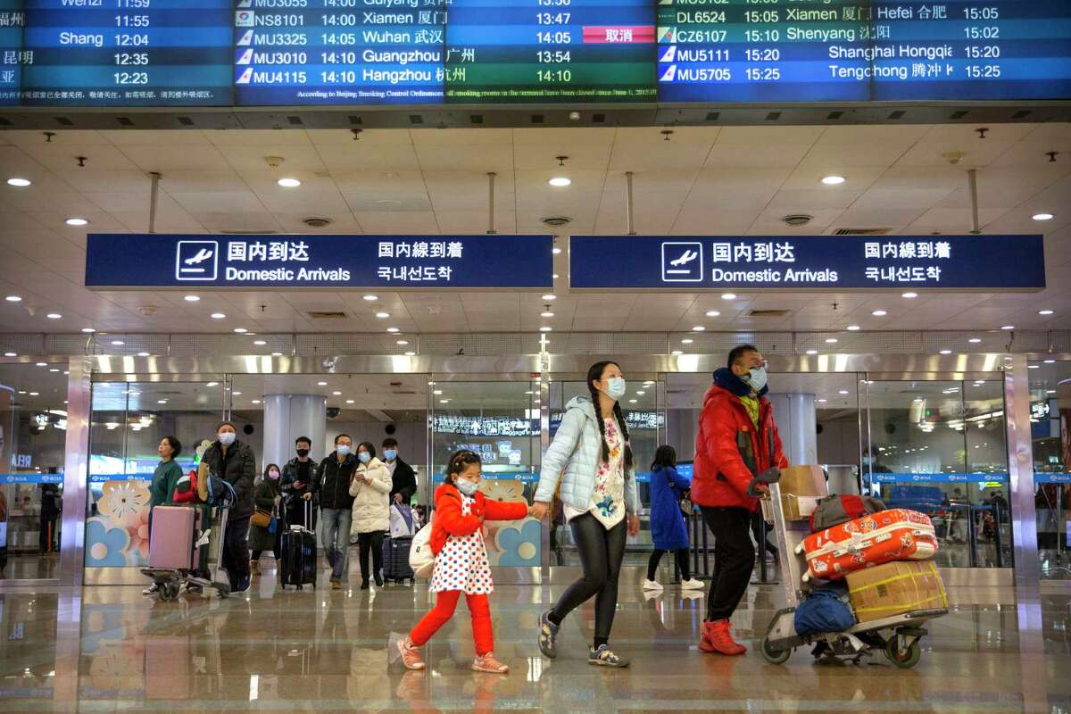 Travelers in face masks walk past a display board showing a canceled flight from Wuhan at Beijing Capital International Airport in Beijing, Thursday, Jan. 23, 2020. China closed off a city of more than 11 million people Thursday, halting transportation and warning against public gatherings, to try to stop the spread of a deadly new virus that has sickened hundreds and spread to other cities and countries in the Lunar New Year travel rush. (AP Photo/Mark Schiefelbein)