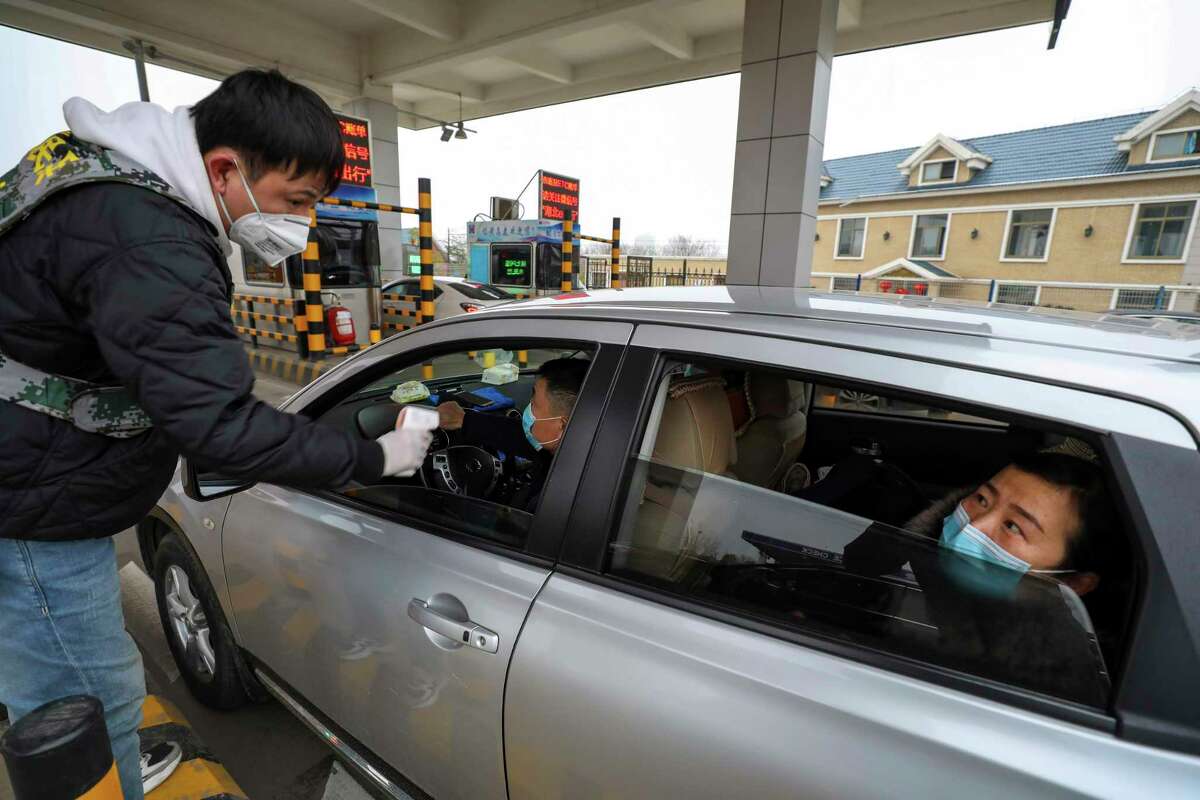 A militia member uses an thermometer gun to take a driver's temperature at a checkpoint at a highway toll gate in Wuhan in central China's Hubei Province, Thursday, Jan. 23, 2020. China closed off a city of more than 11 million people Thursday in an unprecedented effort to try to contain a deadly new viral illness that has sickened hundreds and spread to other cities and countries amid the Lunar New Year travel rush. (Chinatopix via AP)